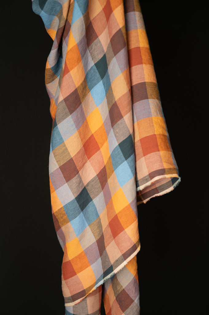 an orange, blue, and brown checkered shirt hanging on a black background